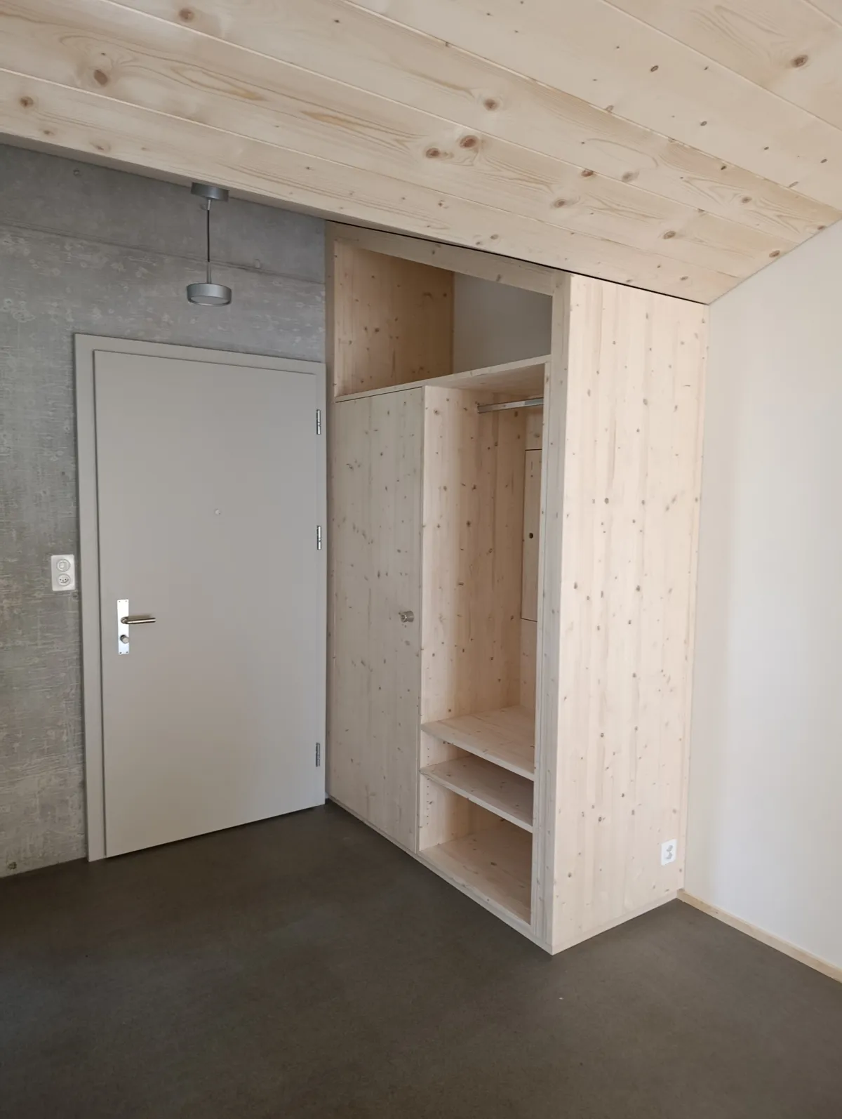 Moderne offene Küche mit rosafarbenen Fronten, Kochinsel und Arbeitsflächen aus Edelstahl. Die helle Holzdecke und die mit Holz verkleidete Fensterwand setzen einen warmen Kontrast zum dunklen Boden und zur modernen Kücheneinrichtung.