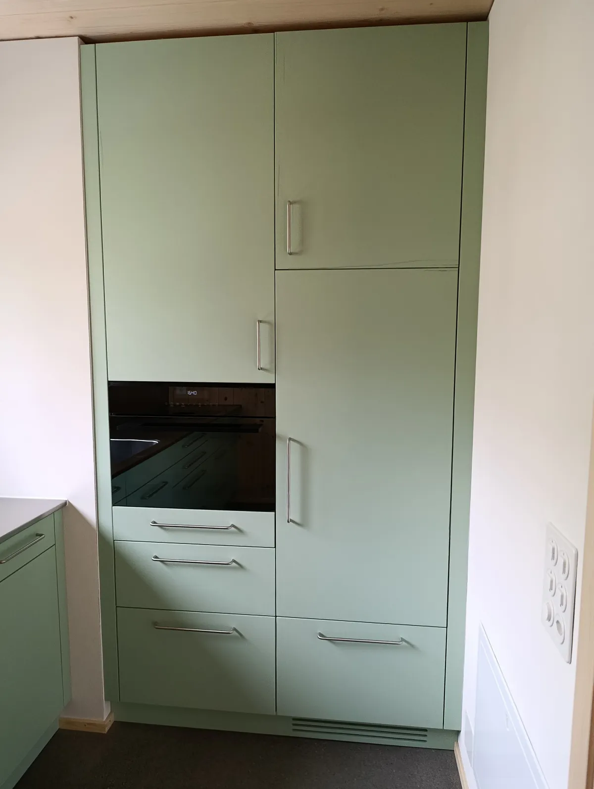 Moderne offene Küche mit rosafarbenen Fronten, Kochinsel und Arbeitsflächen aus Edelstahl. Die helle Holzdecke und die mit Holz verkleidete Fensterwand setzen einen warmen Kontrast zum dunklen Boden und zur modernen Kücheneinrichtung.
