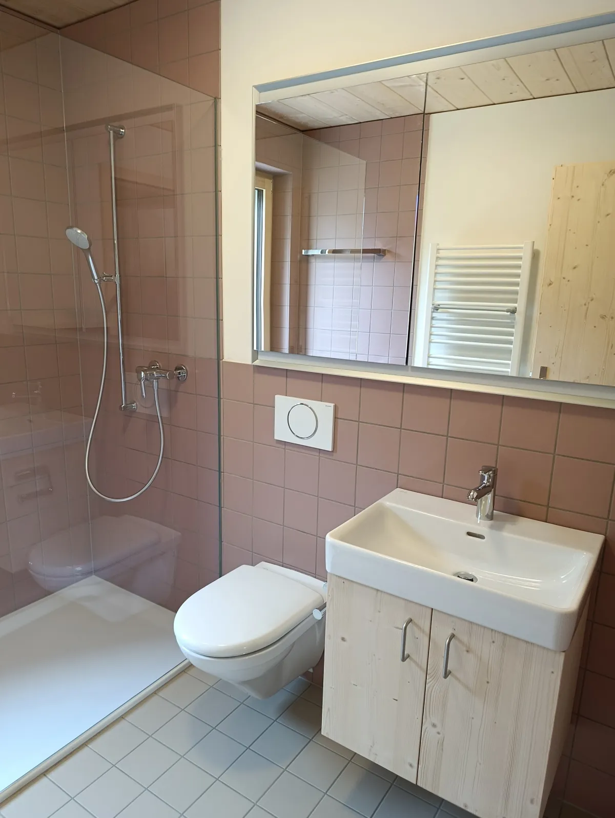 Moderne offene Küche mit rosafarbenen Fronten, Kochinsel und Arbeitsflächen aus Edelstahl. Die helle Holzdecke und die mit Holz verkleidete Fensterwand setzen einen warmen Kontrast zum dunklen Boden und zur modernen Kücheneinrichtung.