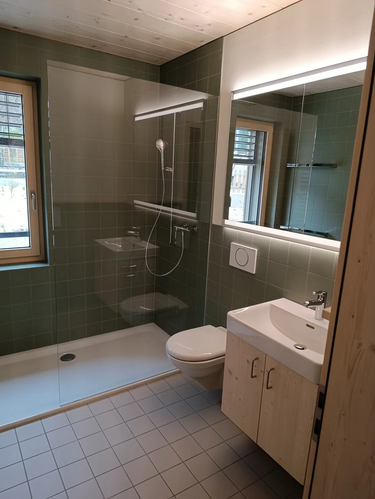 Moderne offene Küche mit rosafarbenen Fronten, Kochinsel und Arbeitsflächen aus Edelstahl. Die helle Holzdecke und die mit Holz verkleidete Fensterwand setzen einen warmen Kontrast zum dunklen Boden und zur modernen Kücheneinrichtung.