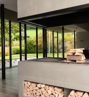 Moderner Essbereich mit grosser Glasfront und Blick in den Garten. In der Mitte steht ein runder Holztisch mit schwarzen Stühlen auf einem hellen Holzboden. Das natürliche Licht schafft eine offene, freundliche Atmosphäre.