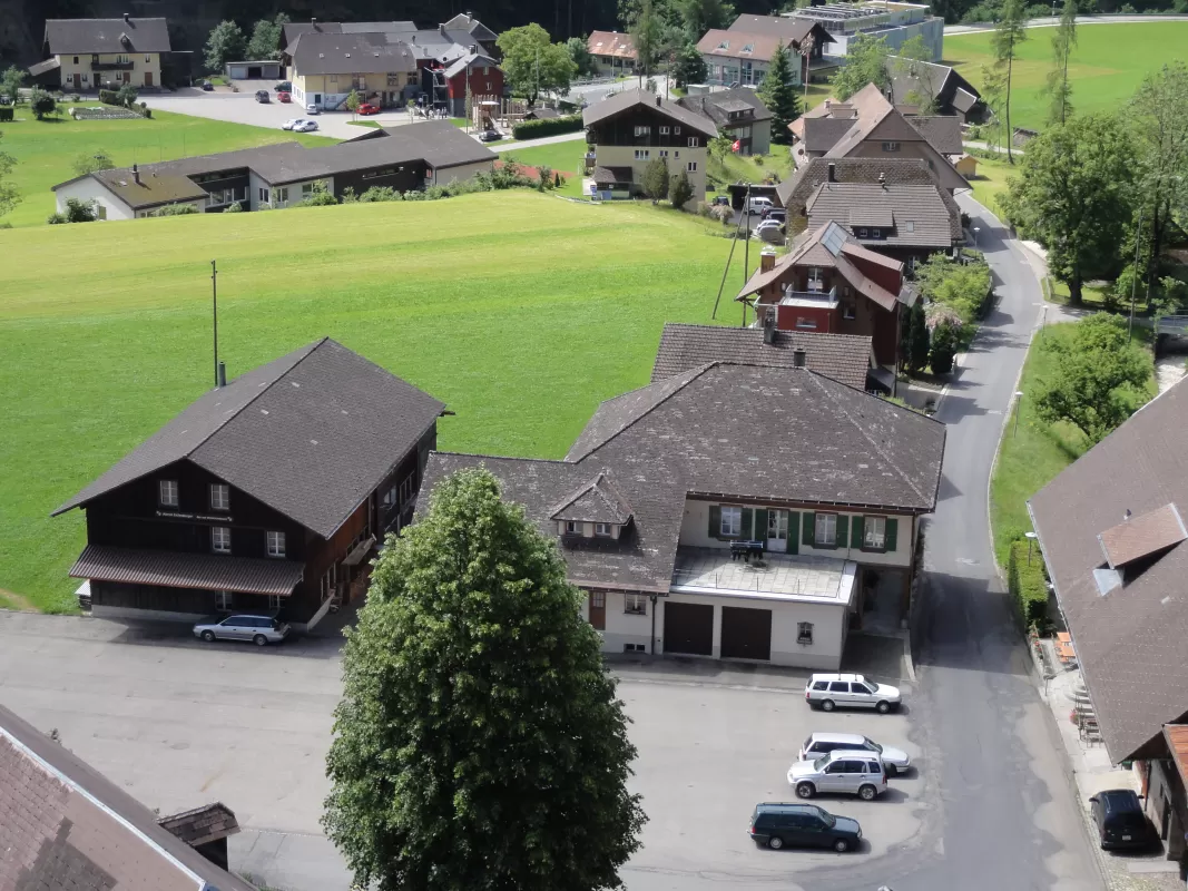 Luftaufnahme des Dorfkerns von Trub im Emmental. Im Vordergrund die Gebäude der Schreinerei Eichenberger mit Werkstatt und Wohnhaus, umgeben von grünen Wiesen, Bäumen und typischen Emmentaler Bauernhäusern entlang einer schmalen Strasse.