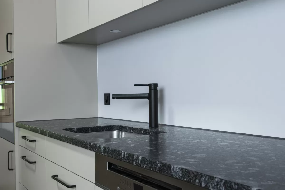 Moderne Küche mit heller Einbauküche, Kochinsel mit Holzarbeitsplatte und integrierten Geräten in einem offenen Wohnraum mit sichtbaren Holzbalken.