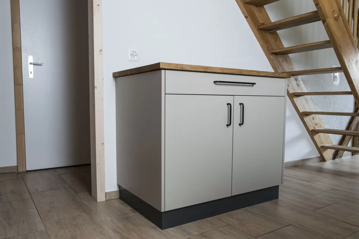 Moderne Küche mit heller Einbauküche, Kochinsel mit Holzarbeitsplatte und integrierten Geräten in einem offenen Wohnraum mit sichtbaren Holzbalken.