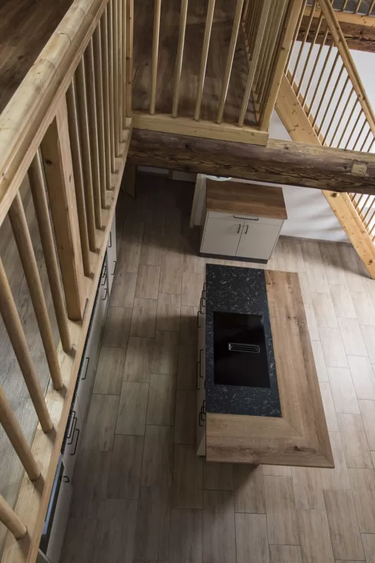 Moderne Küche mit heller Einbauküche, Kochinsel mit Holzarbeitsplatte und integrierten Geräten in einem offenen Wohnraum mit sichtbaren Holzbalken.