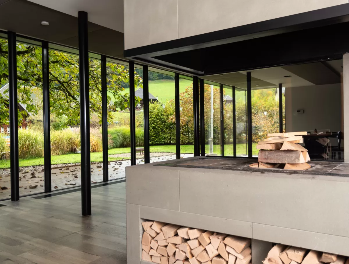 Moderner Essbereich mit grosser Glasfront und Blick in den Garten. In der Mitte steht ein runder Holztisch mit schwarzen Stühlen auf einem hellen Holzboden. Das natürliche Licht schafft eine offene, freundliche Atmosphäre.