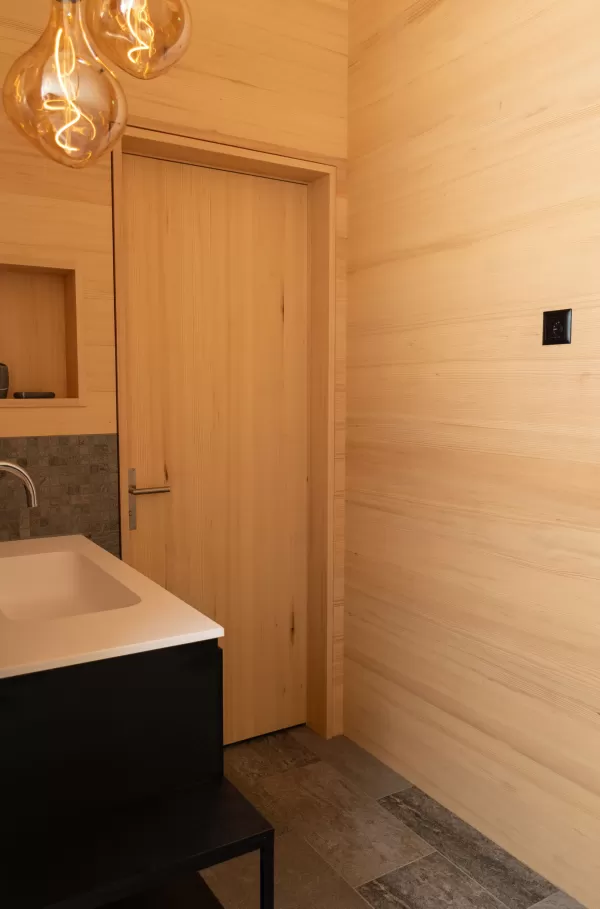 Heller Innenraum mit durchgehendem Holzausbau, Einbauschrank, Sitznische am Fenster und modernem grünen Kaminofen.