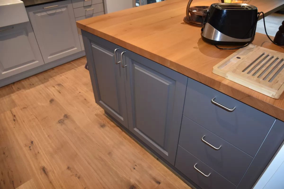 Individuell gestaltete Küche mit hellen Fronten, integrierten Einbaugeräten und grosszügiger Kochinsel mit massiver Holzarbeitsplatte. Der dekorative Fliesenspiegel setzt einen farbigen Akzent und bildet einen Kontrast zu den klaren Linien der Möblierung. Warme Holzböden und die offene Raumgestaltung schaffen eine einladende und wohnliche Atmosphäre.