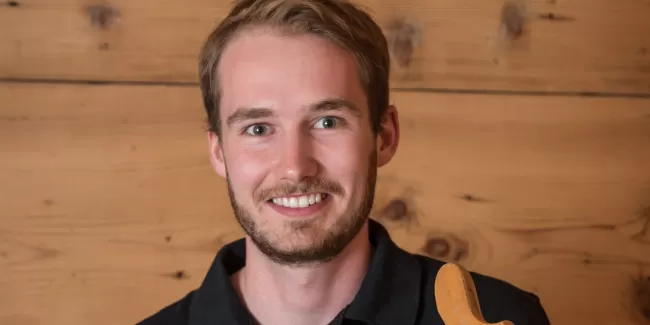 Jan Bucher mit einem alten Werkzeug in der Hand und ein schwarzer Schreinerei Eichenberger Polo Shirt