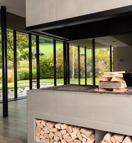 Moderner Essbereich mit grosser Glasfront und Blick in den Garten. In der Mitte steht ein runder Holztisch mit schwarzen Stühlen auf einem hellen Holzboden. Das natürliche Licht schafft eine offene, freundliche Atmosphäre.