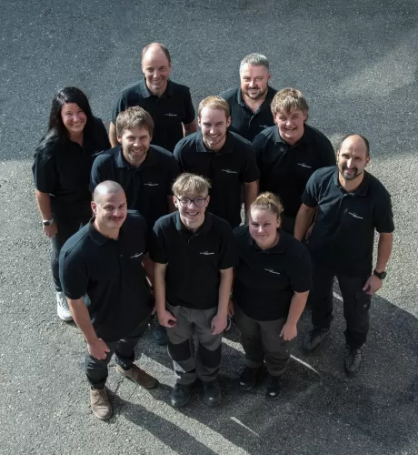 Gruppenfoto des Teams der Zimmerei Hirschi AG: Mitarbeitende in einheitlichen schwarzen Poloshirts stehen im Freien zusammen und blicken lächelnd in die Kamera. Das Bild vermittelt Teamgeist, Zusammenhalt und die persönliche Handschrift des Unternehmens.