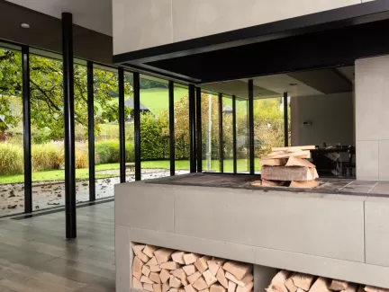 Moderner Essbereich mit grosser Glasfront und Blick in den Garten. In der Mitte steht ein runder Holztisch mit schwarzen Stühlen auf einem hellen Holzboden. Das natürliche Licht schafft eine offene, freundliche Atmosphäre.