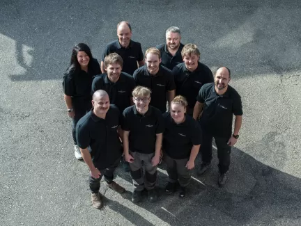 Gruppenfoto des Teams der Zimmerei Hirschi AG: Mitarbeitende in einheitlichen schwarzen Poloshirts stehen im Freien zusammen und blicken lächelnd in die Kamera. Das Bild vermittelt Teamgeist, Zusammenhalt und die persönliche Handschrift des Unternehmens.