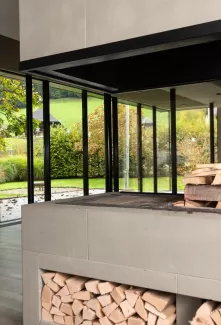 Moderner Essbereich mit grosser Glasfront und Blick in den Garten. In der Mitte steht ein runder Holztisch mit schwarzen Stühlen auf einem hellen Holzboden. Das natürliche Licht schafft eine offene, freundliche Atmosphäre.