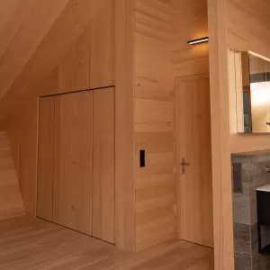 Heller Innenraum mit durchgehendem Holzausbau, Einbauschrank, Sitznische am Fenster und modernem grünen Kaminofen.