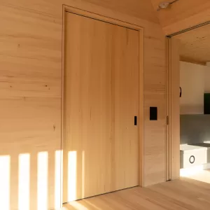 Heller Innenraum mit durchgehendem Holzausbau, Einbauschrank, Sitznische am Fenster und modernem grünen Kaminofen.