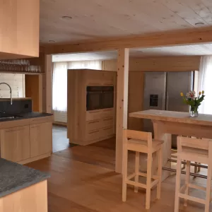 Moderne Holzküche mit grauer Arbeitsplatte, Einbauspüle und indirekter Beleuchtung in einem warmen Holzinnenraum.