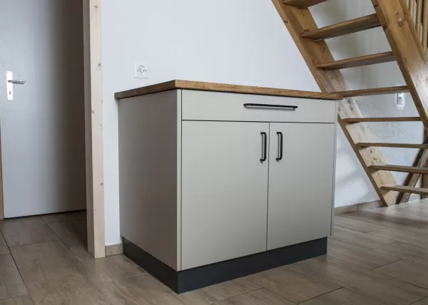 Moderne Küche mit heller Einbauküche, Kochinsel mit Holzarbeitsplatte und integrierten Geräten in einem offenen Wohnraum mit sichtbaren Holzbalken.