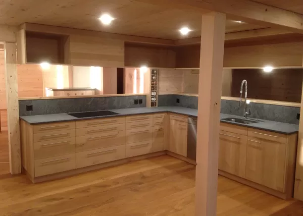 Moderne Holzküche mit grauer Arbeitsplatte, Einbauspüle und indirekter Beleuchtung in einem warmen Holzinnenraum.