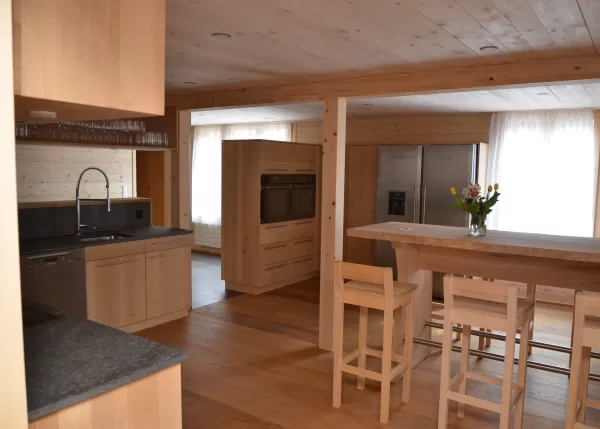 Moderne Holzküche mit grauer Arbeitsplatte, Einbauspüle und indirekter Beleuchtung in einem warmen Holzinnenraum.