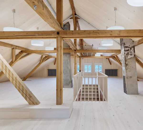 Für dieses Bild würde ich den Alt-Text so formulieren:  "Heller, mit Holz ausgekleideter Schulraum mit Fischgrätparkett, Kassettendecke, grossen Fenstern, Hängeleuchten und einer grünen Wandtafel.